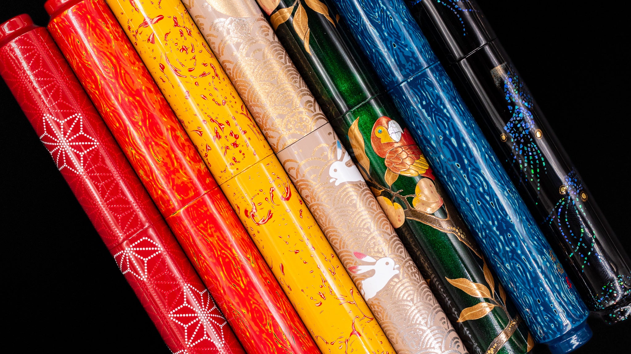 Set of colorful urushi fountain pens with intricate designs on a black background