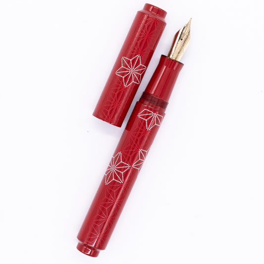 An overhead view of the AP Limited Editions Sakura Lacquer Art Fountain Pen - Snowflakes Red uncapped, with the cap next to the body angled towards the right.