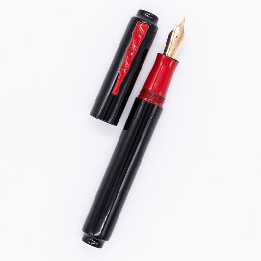 An overhead view of the AP Limited Editions Urushi Lacquer Art Fountain Pen - Black & Red uncapped, with the cap next to the body angled towards the right.